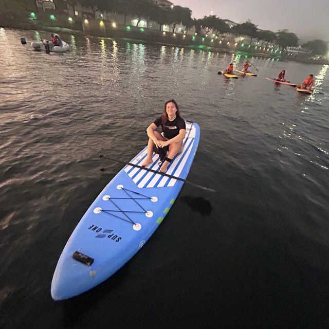 Eduarda, autora do Quero Mochilar, sentada em uma prancha de stand up paddle em um lago ao entardecer